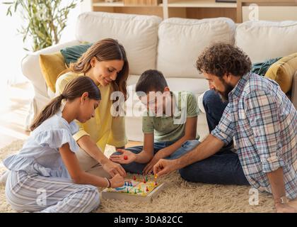 Die Familie versammelt sich in einem gemütlichen Wohnzimmer und spielt gemeinsam ein Brettspiel, voller Lachen und Lächeln Stockfoto