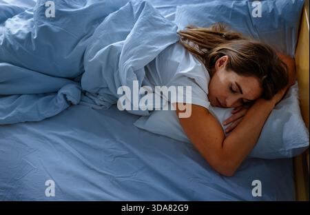 Eine Frau ruht nachts in einem Schlafzimmer, bedeckt mit einer Decke, schläft auf dem Bauch Stockfoto