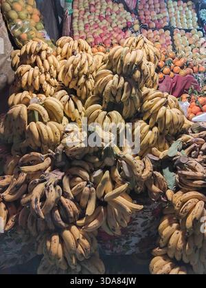 Gelbe Bananen und verschiedene saisonale Früchte werden an einem traditionellen Straßenmarkt ausgestellt. Stockfoto