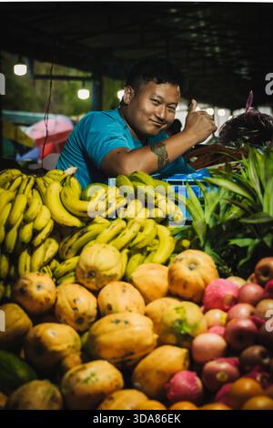 Paro, Bhutan - 17. September 2025: Blick auf einen Verkäufer inmitten einer lebhaften Ausstellung von Bananen, Papayas und Pflaumen, die eine farbenfrohe und üppige Ernte präsentieren Stockfoto