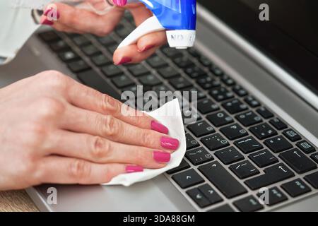 Frau Reinigung Laptop-Tastatur mit weißem Gewebe, Detail an ihren Fingern hält Papiertuch, blauen Alkohol Sprayer in der Nähe - Desinfektion Konzept Stockfoto