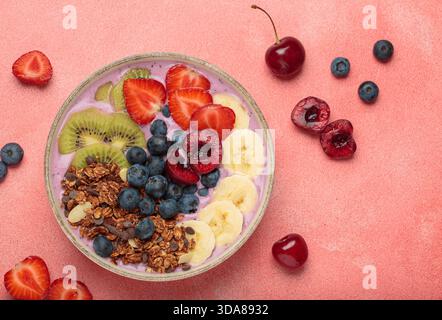 Lebendige und nahrhafte Acai-Schüssel mit geschnittenem Kiwi, Erdbeeren, Heidelbeeren, Kirschen, Banane, und Müsli, eine bunte und gesunde Mahlzeit oder ein Frühstück auf rosa Hintergrund Stockfoto