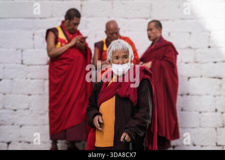 Thimphu, Bhutan - 28. September 2025: Blick auf eine ältere Frau mit Maske und Stock fällt vor dem Hintergrund des weißen Steingebäudes hervor. Stockfoto