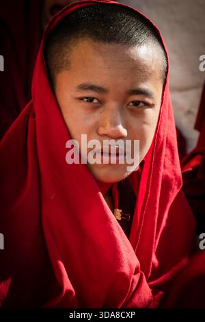 Thimphu, Bhutan - 28. September 2025: Blick auf das ruhige Gesicht eines jungen Mönchs, eingerahmt von den leuchtenden roten Gewändern, ein Porträt der Hingabe und des Friedens. Stockfoto