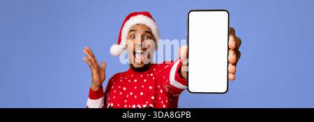 Der aufgeregte Mann im Weihnachtspullover zeigt das Smartphone in festlicher Umgebung Stockfoto
