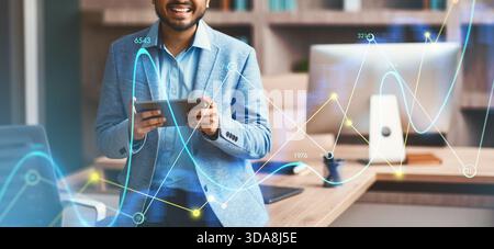 Lächelnder indischer Geschäftsmann, der selbstbewusst auf einem digitalen Tablet in modernen Büroumgebungen surft Stockfoto