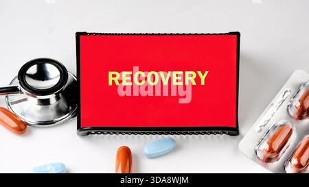 Farbenfrohes Zeichen, das das Wort Recovery zeigt, ist neben einem Stethoskop und verschiedenen Kapseln gesetzt, die Hoffnung und Heilung in einem medizinischen Kontext symbolisieren. Stockfoto