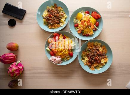 Salat- und Nudelteller mit verschiedenen frischen Gemüsesorten, ordentlich auf Holztisch angeordnet Stockfoto