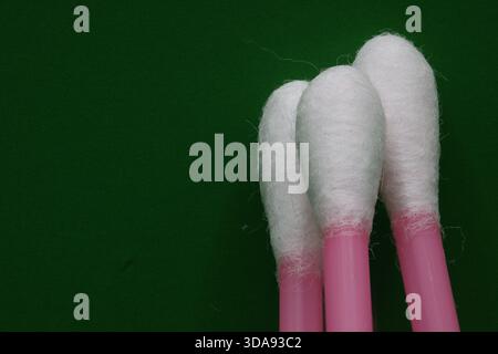 Nahaufnahme von drei rosafarbenen Wattestäbchen mit weißen Baumwollspitzen auf dunkelgrünem Hintergrund. Stockfoto