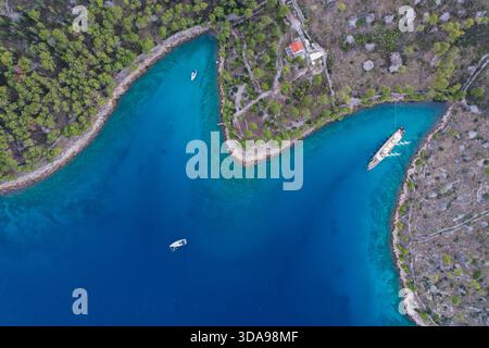 Aus der Vogelperspektive auf das türkisfarbene Wasser entlang der grünen Küste mit Booten, Milna, Split-Dalmatien County, Kroatien. Stockfoto