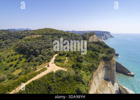 Blick aus der Vogelperspektive auf dramatische Klippen, die in das türkisfarbene Meer stürzen, üppiges Grün im Kontrast zur zerklüfteten Küste, Kap Drastis, Korfu, Griechenland. Stockfoto