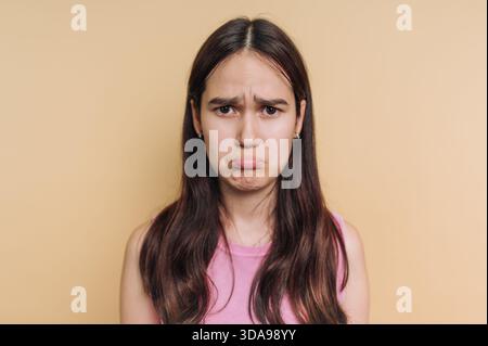 Junge Frau mit langen Haaren, die vor beigefarbenem Hintergrund schmeichelt. Stockfoto