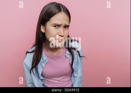Junge Frau mit skeptischem Ausdruck vor rosa Hintergrund. Stockfoto