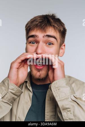 Junger Mann, der mit den Händen um den Mund schreit, aufgeregter Ausdruck Stockfoto