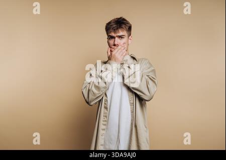 Junger Mann, der den Mund mit Händen bedeckt, überraschter Ausdruck Stockfoto