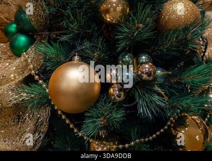 Weihnachtstannenzweige mit glänzendem Gold und tiefgrünen Kugeln verziert, die einen festlichen saisonalen Hintergrund schaffen Stockfoto