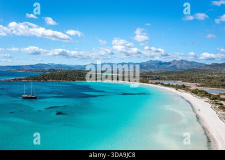 Eine ruhige Küstenszene mit einem einsamen Segelboot auf lebhaftem türkisfarbenem Wasser, einem geschwungenen weißen Sandstrand, Sardinien, Italien Stockfoto