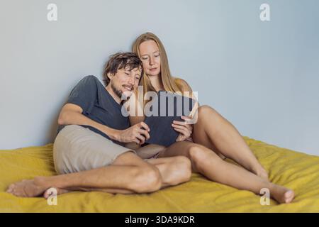 Frau und Mann entspannen sich auf einem Bett, während sie auf ein Tablet schauen und eine ruhige Morgenatmosphäre genießen. Lebensstil, Technologienutzung und Zusammengehörigkeit Stockfoto