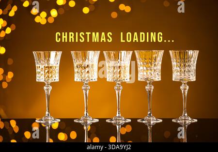 Weihnachtsladung, Feiertagserwartung. Gläser mit Wein und zwei leere vor goldenem Hintergrund mit Bokeh-Lichtern Stockfoto
