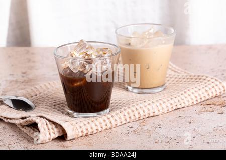 Zwei Kaffeegetränke, Eiskaffee und schwarzer Espresso auf beigefarbenem, strukturiertem Hintergrund Stockfoto