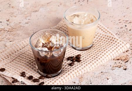 Eiskaffee und schwarzer Kaffee serviert in klaren Gläsern auf beigefarbenem Steintisch, Nahaufnahme Stockfoto