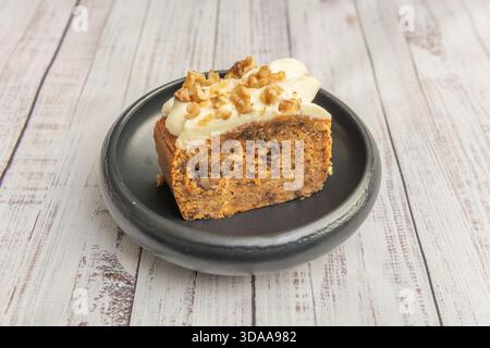 Karottenkuchen mit Walnüssen und Rosinen, garniert mit einem großzügigen Frischkäse-Frosting, dekoriert mit karamelisierten Pekannüssen und einem Stäuben von gemahlenem Zimt Stockfoto
