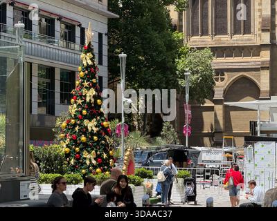 Melbourne, VIC, Australien. Dezember 2025. - Ein geschmückter Weihnachtsbaum steht prominent auf einem belebten Stadtplatz, umgeben von verschiedenen Menschen, m Stockfoto
