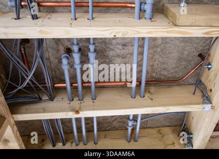 Nahaufnahme der Installationen von Sanitär- und Elektrorohren hinter Holzrahmen in einer unfertigen Decke Stockfoto