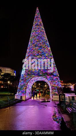 Während einer Feiertagsfeier in Bournemouth, Großbritannien, Dezember 2022, laufen die Menschen unter einem großen, beleuchteten Bogen in Form eines Weihnachtsbaums mit bunten Lichtern Stockfoto