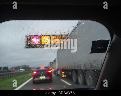 Brescia, Italien 21. November 2025 Autobahnstau auf der A21 in der Nähe von Cremona im regnerischen Winter, Blick durch die Windschutzscheibe des nassen Autos mit leuchtenden Warnern Stockfoto