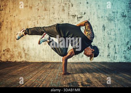 Junger Mann, der auf Wandhintergrund tanzt. Lebendige Farbeffekte. Tätowierung am Körper Stockfoto