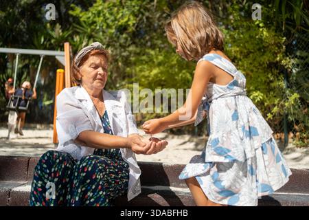 Mädchen mit den Händen, die auf dem Spielplatz Sand ausgießen, genießen den Moment, in dem Sand aus der Hand fließt, und schaffen eine lustige und aktive Szene im Freien Stockfoto