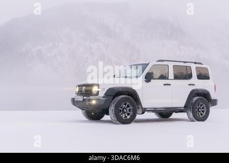 Krasnojarsk, 10. Januar 2025: Weißer SUV mit Allradantrieb Tank 300 in der Natur. Schneebedeckte Berge im Hintergrund Stockfoto