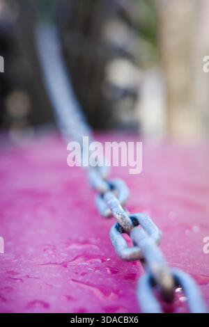 Metallkette auf nassrosa Oberfläche mit geringer Schärfentiefe Stockfoto