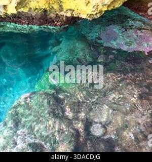 Klares türkisfarbenes Meerwasser schimmert unter der felsigen Höhle an der Küste der Insel Korfu, Griechenland. Sonnenlichtreflexionen auf dem Flachwasser Stockfoto