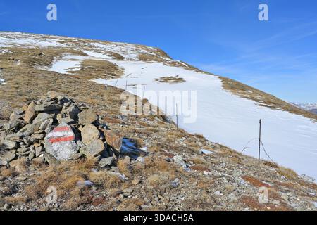 Cairn mit rot-weißer Wegmarkierung, die einen Pfad in einer herbstlichen Berglandschaft anzeigt Stockfoto