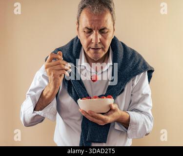 Porträt eines gutaussehenden älteren Mannes, der einen frischen Salat mit einer Kirschtomate auf seiner Gabel isst. Das Konzept der gesunden Ernährung, der mediterranen Ernährung und des aktiven Rev Stockfoto