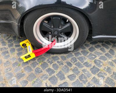 Ein klassischer schwarzer Porsche in Deutschland hat sein seltenes Rad, das durch eine hellgelbe und rote Radklemme auf einer kopfsteingepflasterten Straße blockiert wird. Foto Willy Matheisl Stockfoto