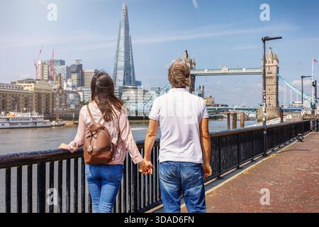 Ein paar Spaziergänge am Flussufer der Themse in London, England, mit Blick auf die Tower Bridge und die Skyline an einem Sommertag Stockfoto