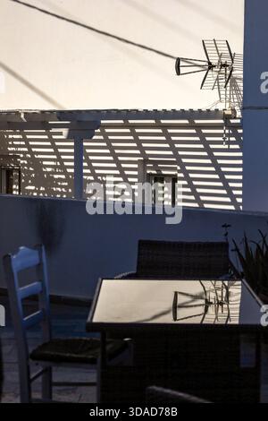 Eine minimalistische Outdoor-Szene mit einer weißen Wand mit starken linearen Schatten von einer Pergola und einer Antenne. Stockfoto