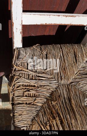 Ein alter Korbsitz mit sichtbaren Verschleißmustern steht im Kontrast zu einem verwitterten lackierten Rahmen, der rustikalen Charme und haptische Schönheit unterstreicht. Stockfoto