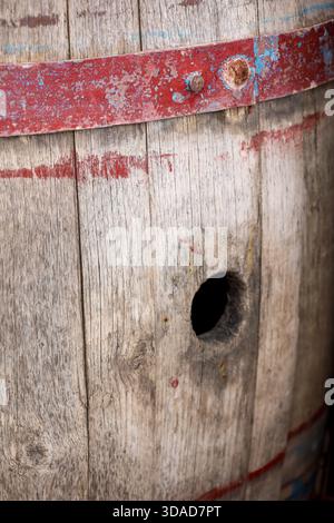 Nahaufnahme eines alten Holzfasses mit verblassten rot lackierten Bändern, gebrochenem Holzkorn und einer dunklen Lochöffnung. Stockfoto
