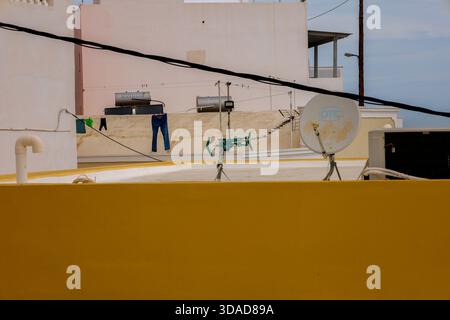 Santorini, Griechenland - 1. November 2025. Städtische Dachszene mit Solaranlagen, Wäscherei, Satellitenschüsseln und farbenfrohen Gebäudewänden Stockfoto