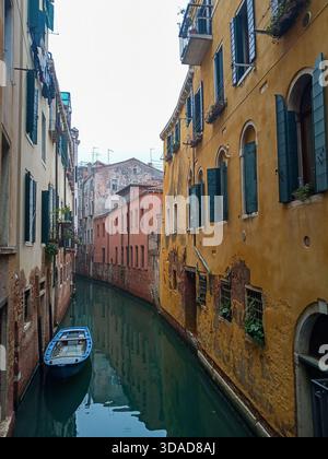 Venedig, Italien - 8. Dezember 2025. Eine friedliche Kanalszene in Venedig mit alten, farbenfrohen Fassaden und einem kleinen blauen Boot Stockfoto