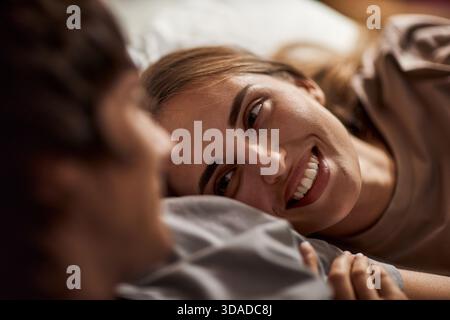 Junge Frau Lächelt, Während Sie Drinnen Neben Dem Jungen Mann Liegt Stockfoto