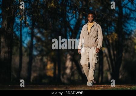 Mann, der durch einen Herbstwald läuft, trägt beige Jacke und Cargo Hosen im Herbstlicht Stockfoto