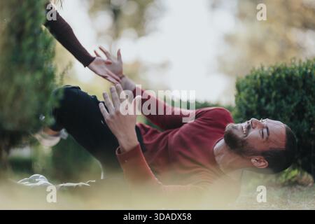 Glücklicher Mann in rotem Pullover, der auf Gras im Park liegt und nach einer High Five greift Stockfoto