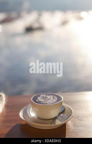 Entspannendes Kaffeetassen-Getränk am Morgen auf Holztisch. Der wunderschöne Meerblick im Hintergrund bietet einen ruhigen und ruhigen Moment, um den Tag mit in zu beginnen Stockfoto