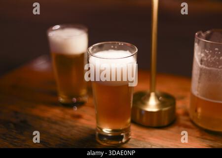 Zwei Glasbehälter mit Bier und Schaum auf Holztisch in der Bar. Die warme Lampe sorgt für ein gemütliches und entspannendes Licht für einen perfekten Abend mit erfrischendem dr Stockfoto
