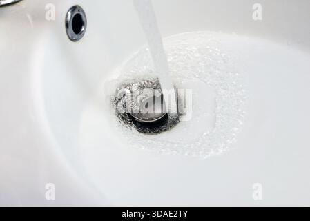 Wasser läuft vom Wasserhahn in das Waschbecken im Bad, Nahaufnahme. Stockfoto